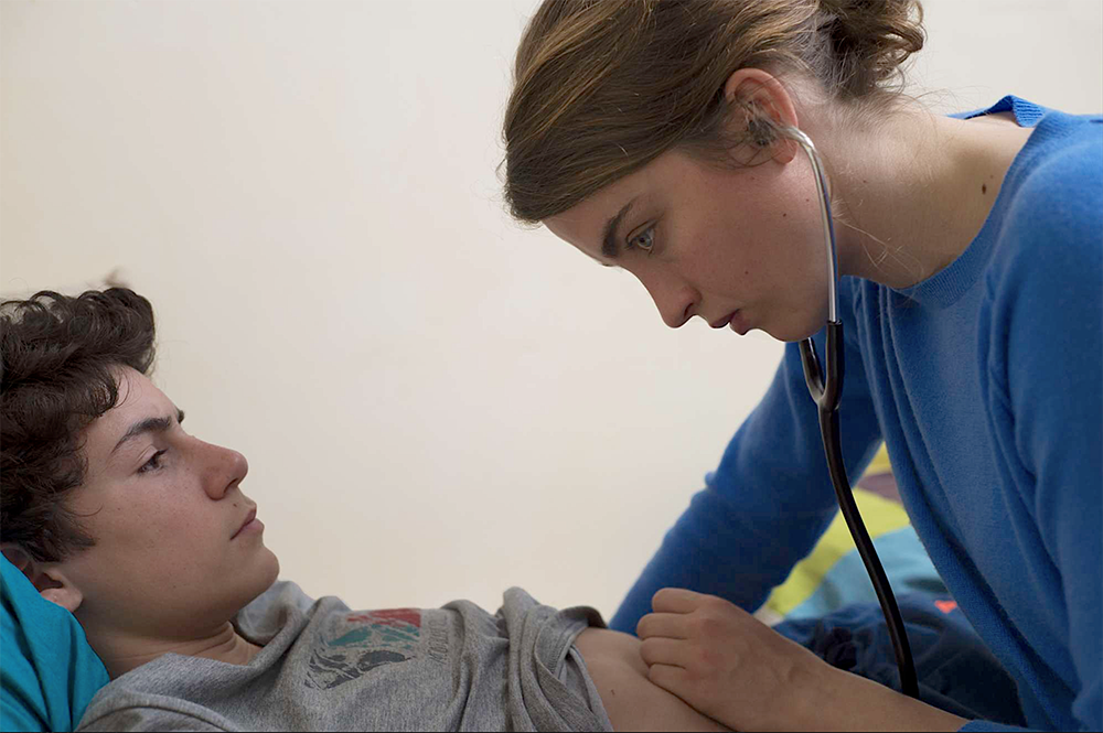 Filmscene uit La fille inconnue: arts onderzoek jonge patiënt met een stetoscoop op zijn buik